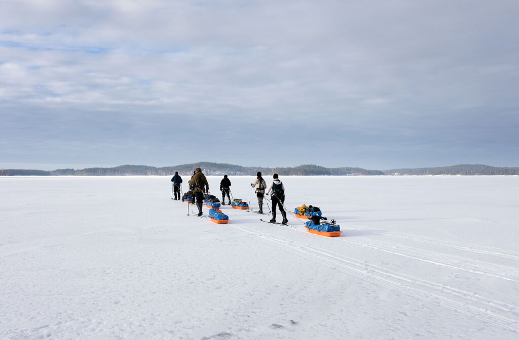 Ryhmä retkeilijöitä jäällä, vetävät ahkioita perässä.