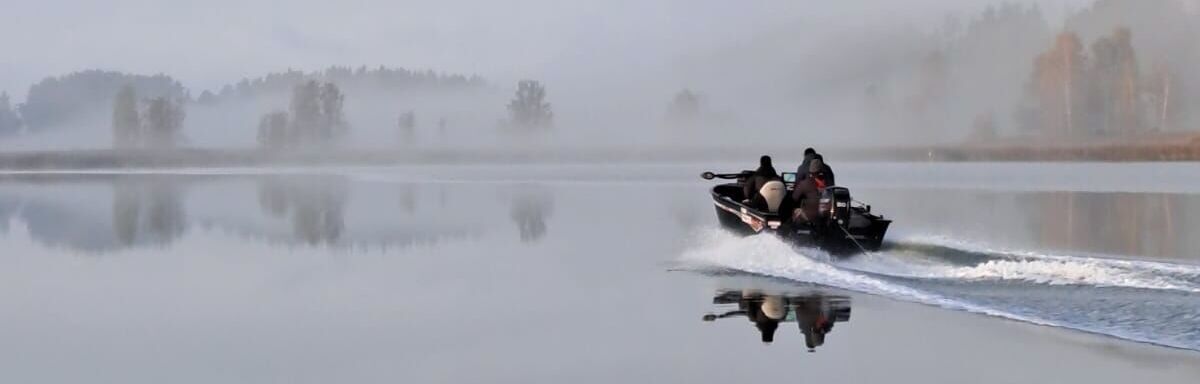 Pieni moottorivene ajamassa sumuisessa saaristomaisemassa.