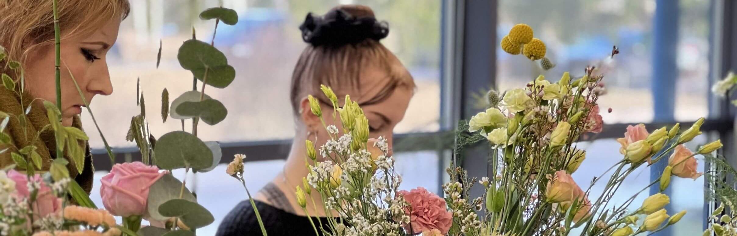 Kaksi floristiopiskelijaa kukkamaljakoiden takana työskentelemässä.