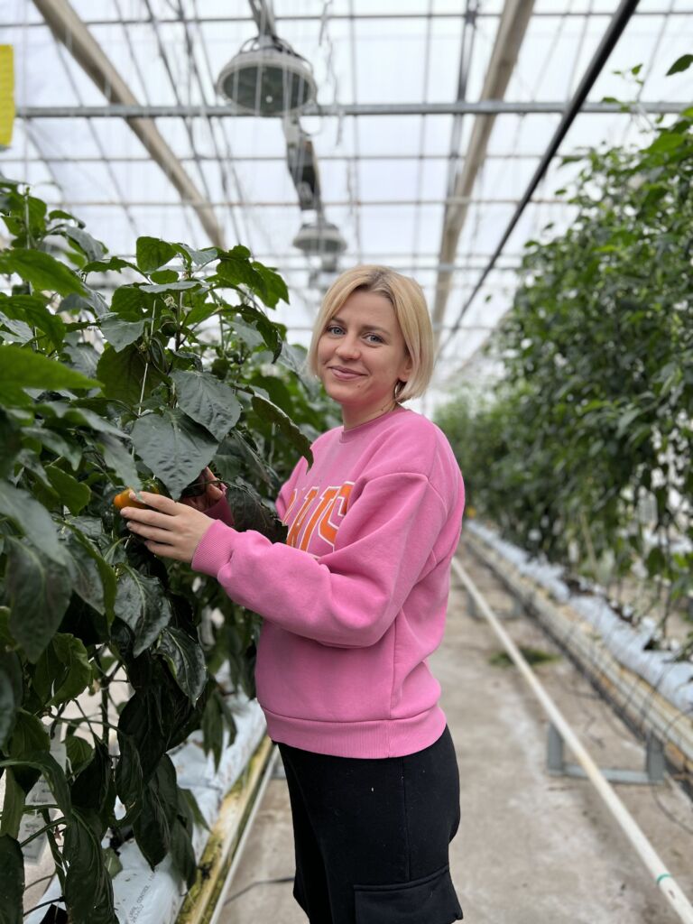 IMG_8625 A person stands next to a large-leaved plant in a greenhouse.