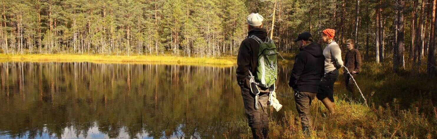 Ympäristönhoitajaopiskelijat metsälammen rannalla seisomassa.