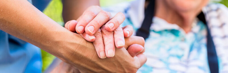 Vanhus pitämässä kiinni hoitajan kädestä.