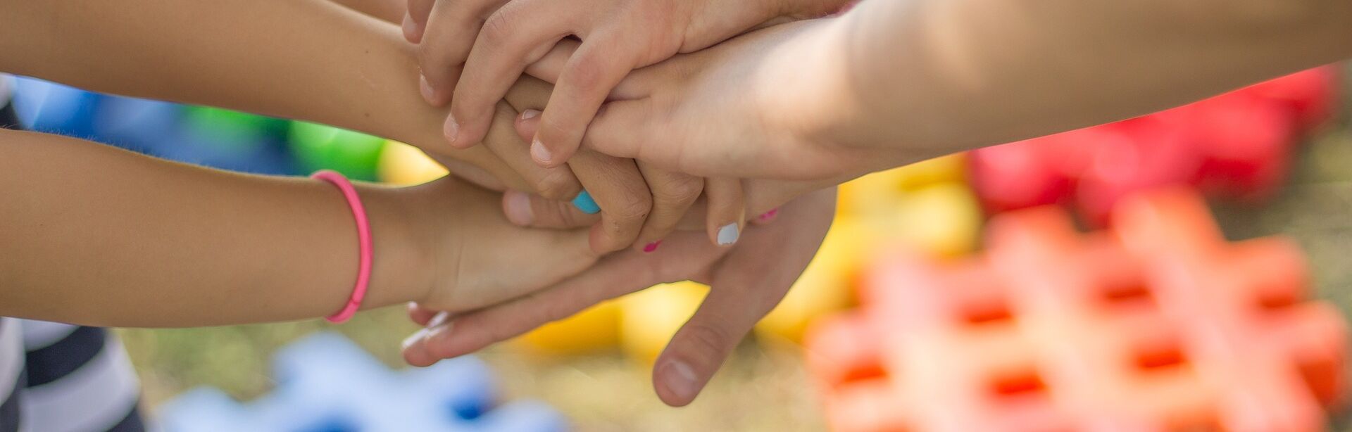 Joukko käsiä pitämässä toisista kiinni, taustalla värikkäitä palikoita.