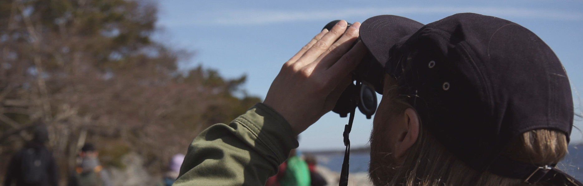 Lippispäinen henkilö takaapäin kiikaroimassa taivaalle.